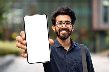 Cheerful young indian guy showing smartphone with white blank screen