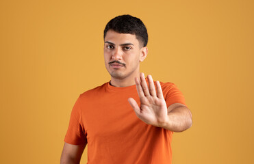 Rejection. Discontented brazilian man gesturing stop with hand, disapproving and refusing bad offer, yellow background