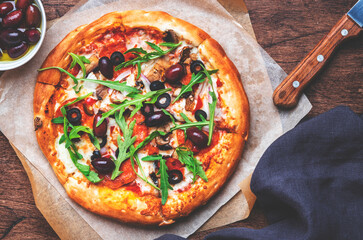 Homemade Pizza with sausage, cheese, mushrooms, olives, tomato sauce and arugula, rustic wooden table background, top view