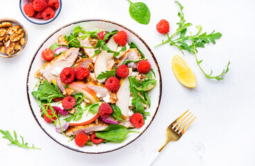 Delicious salad with raspberries, grilled chicken, pears, white cheese, onions, walnuts, spinach and mixed herbs, white table background, top view