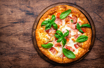 Hot pizza with ham, pancetta, mozzarella cheese, tomato sauce and green basil, rustic wooden table background, top view