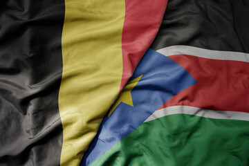 big waving national colorful flag of belgium and national flag of south sudan .