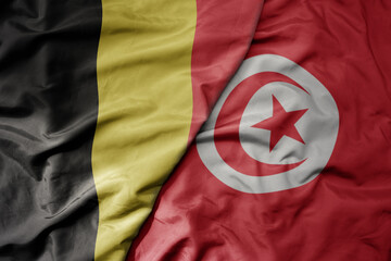 big waving national colorful flag of belgium and national flag of tunisia .
