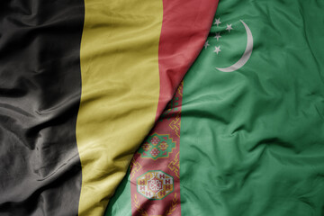 big waving national colorful flag of belgium and national flag of turkmenistan .