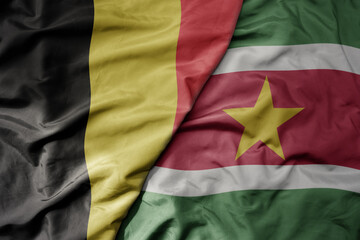 big waving national colorful flag of belgium and national flag of suriname .