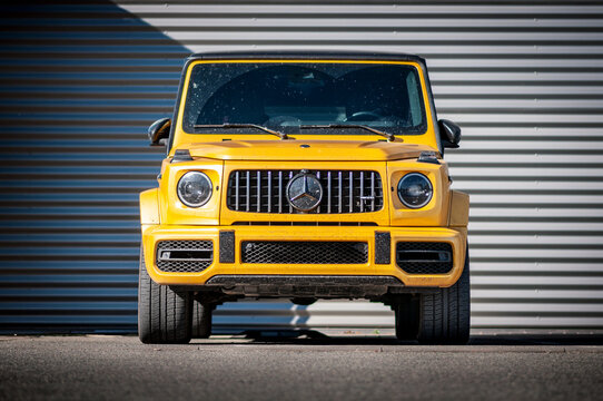 Brno, Czech Republic - September 6, 2023: A yellow off-road Mercedes Benz G-class luxury SUV is parked in front of a corrugated metal wall in an industrial zone.