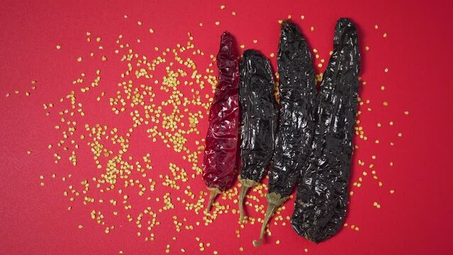 Placing dried mexican chili appearing one by one on red surface with seeds