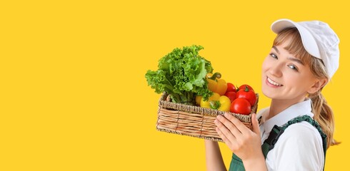 Young female farmer with wicker basket full of different vegetables on yellow background with space for text