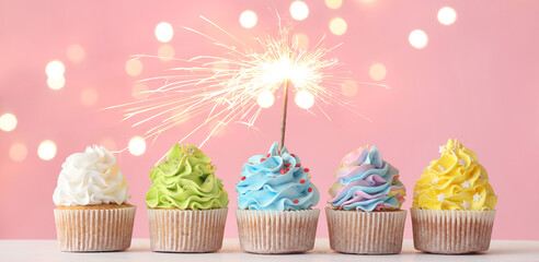 Tasty cupcakes with sparkler on pink background