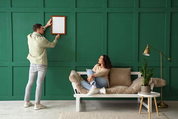Young couple hanging blank frame on green wall at home