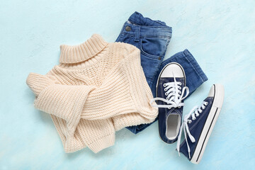 Knitted children's sweater, jeans and gumshoes on color background