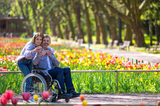 Middle aged wife and disabled husband in wheelchair walking in park.