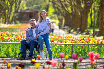 Middle aged wife and disabled husband in wheelchair walking in park.
