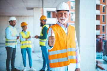 An engineer giving OK sign at construction site. Portrait of happy architect with clipboard gesturing thumbs up outside building. Smiling architect in a construction site