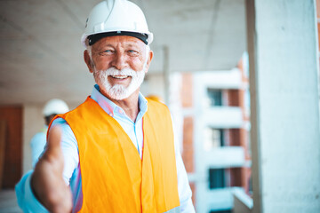 Portrait of a Construction Manager . He offers his hand for the conclusion of a new business, behind him construction workers watching plans with architect.