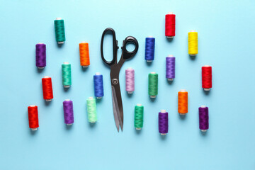 Composition with different thread spools and scissors on color background