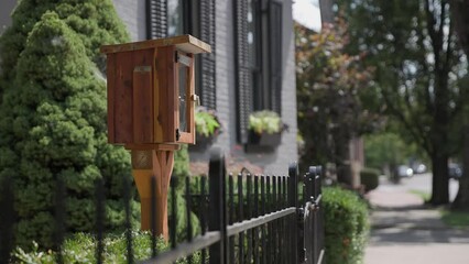 Handheld slow motion view of library book exchange box made of wood in suburban middle class neighborhood to be read, traded, and discussed by public