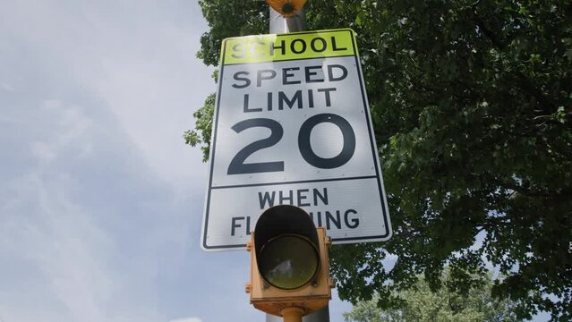 Handheld slow motion view of a school 20 miles per hour when flashing mph speed limit sign near educational building in suburb