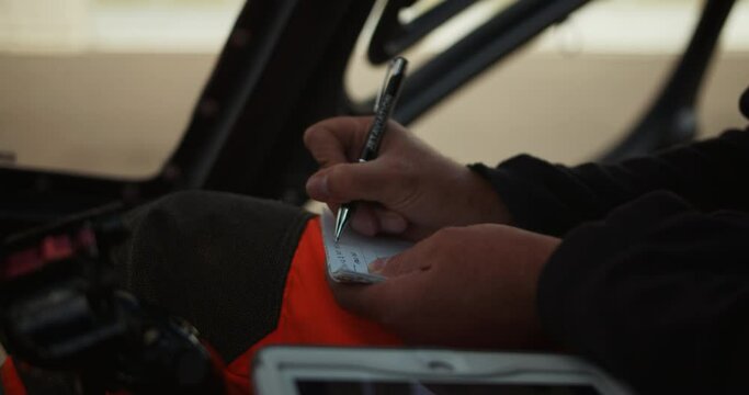 Detailed view of male hands writing text on paper. Filling out mandatory documents before take off. Pilot performing preflight procedure in helicopter cockpit. Airport and aviation concept