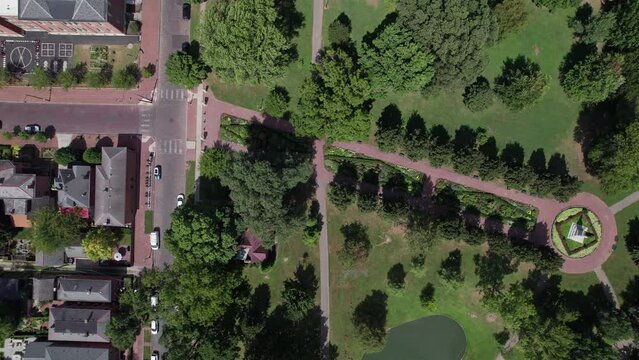 Drone shot of German Village public grounds, outdoor theater, water pond, recreational center, and walking sidewalks with trees and gardens at Schiller Park near downtown Columbus, Ohio