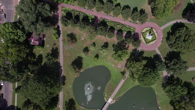 Drone shot of German Village public grounds, outdoor theater, water pond, recreational center, and walking sidewalks with trees and gardens at Schiller Park near downtown Columbus, Ohio