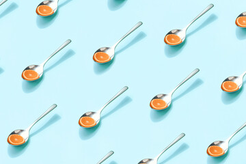 Pattern of spoons with orange slices on isolated light blue background. Summer fruit diet. Minimal summer fruit concept. Citrus sources of carotenoids, flavonoids and vitamin c.