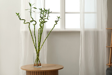 Vase with bamboo stems on table near window