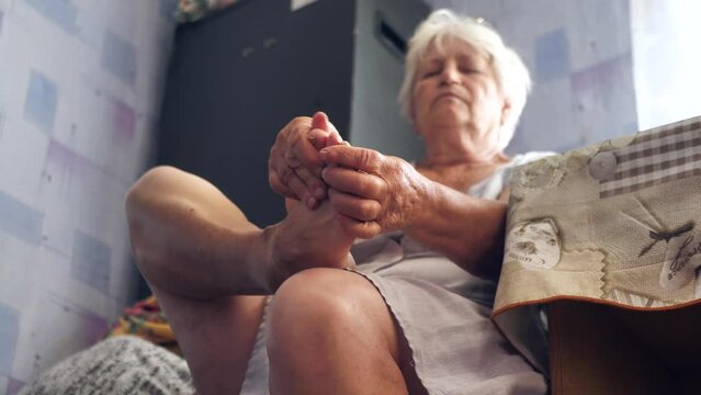 An old woman of 70 massages her leg, making the skin of her legs smooth, slow motion.The concept of podology. inflammatory diseases of the ligaments of the foot
