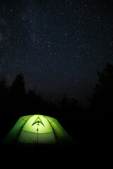 Night sky with bright stars and green tent on the top of the mountain. Camping.