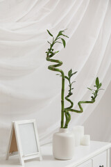 Vase with bamboo stems and blank picture frame on table against white fabric background