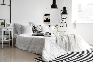 Cozy bed with white blanket and pillows in interior of stylish bedroom