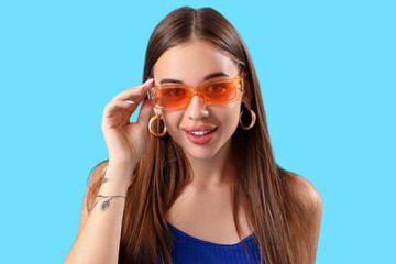 Stylish young woman in sunglasses on blue background, closeup