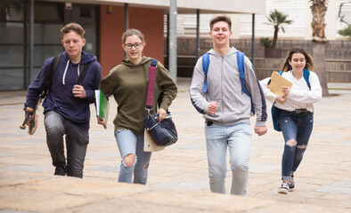 Fototapeta premium Group of cheerful students running along the city street