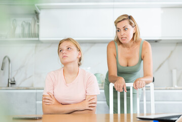 Upset teenage girl sitting in home kitchen, forced to listen to reprimands of disgruntled mother....