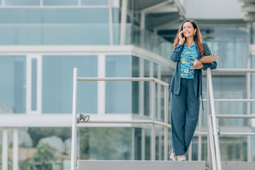 Fototapeta premium business woman talking on mobile phone in the street with office background