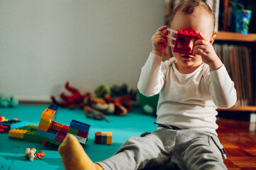 A cute little toddler is expanding his imagination and looking through the window plastic brick toy...