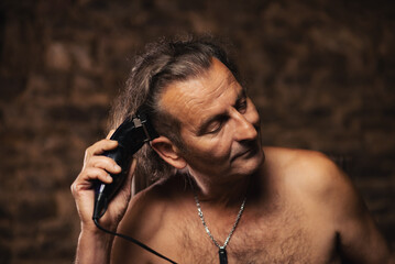 An older man, about 60 years old, of Serbian nationality cuts his own hair with a clipper.
