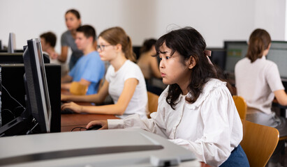 Portrait of fifteen-year-old schoolgirl studying at computer in a class at an informatics lesson with classmates
