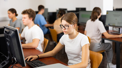 Fototapeta premium Young girl student with glasses studying on computer in college library, concept of education