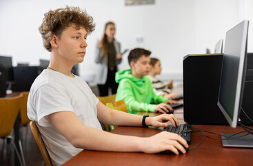 Fototapeta premium Teenage caucasian boy learning to use personal computer during lesson in school.