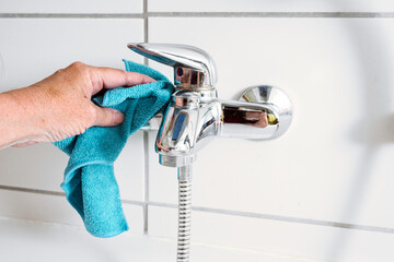 Cleaning a bathtub faucet with a blue microfiber cloth to remove limescale stains from hard calcium...
