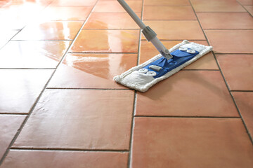 Flat wet-mop made of microfiber wipes the tiled terracotta floor, daily cleaning routine for a...
