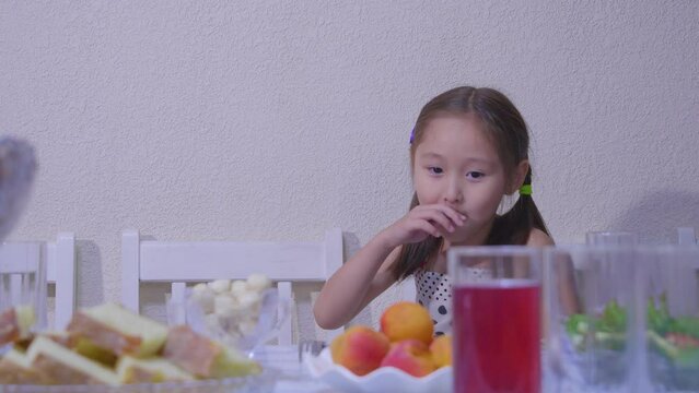 A cute girl picks up a fruit, points to the camera and eats
