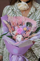 Woman holds beautiful bright bouquet with beautiful flowers and colored branches packed in wrapping paper. Valentine's, women's, mother's day, 8th of march. 14th of february. Teacher's.