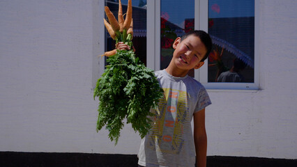 A teenager holds a carrot in his hands and smiles