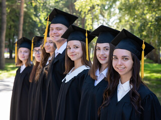 Row of happy young people in graduation gowns outdoors. Students in the park.