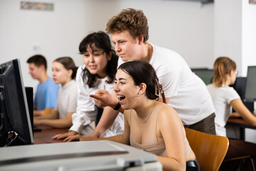 Amazed teenagers giving a clue to the amazed female classmate while she is using PC in the computer classroom