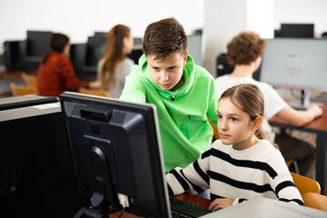 Teenager guy helps girl solve problem on computer in a school class