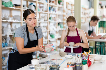 Young woman teacher in apron sculpts ceramic product from clay in ceramic workshop