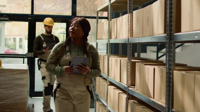 Revealing shot of woman in warehouse inputing updated products info on online shopping website using tablet, walking through retail storage hub aisles checking labels on wares